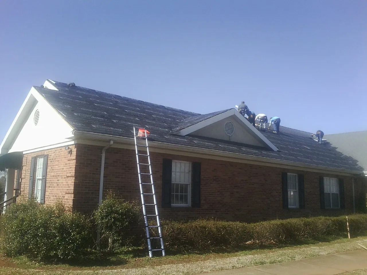 Crew tearing shingles off a brick ranch roof with a ladder set — Emergency Roof Repair work by our crew in Southport