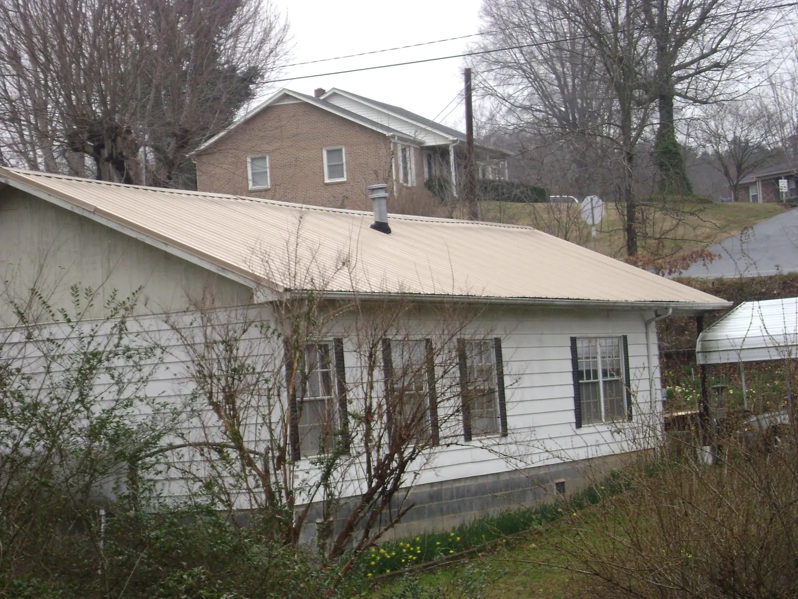 Tan metal roof on a white sided house set into a hillside — Commercial Roofing by Roofing Brothers in Southport